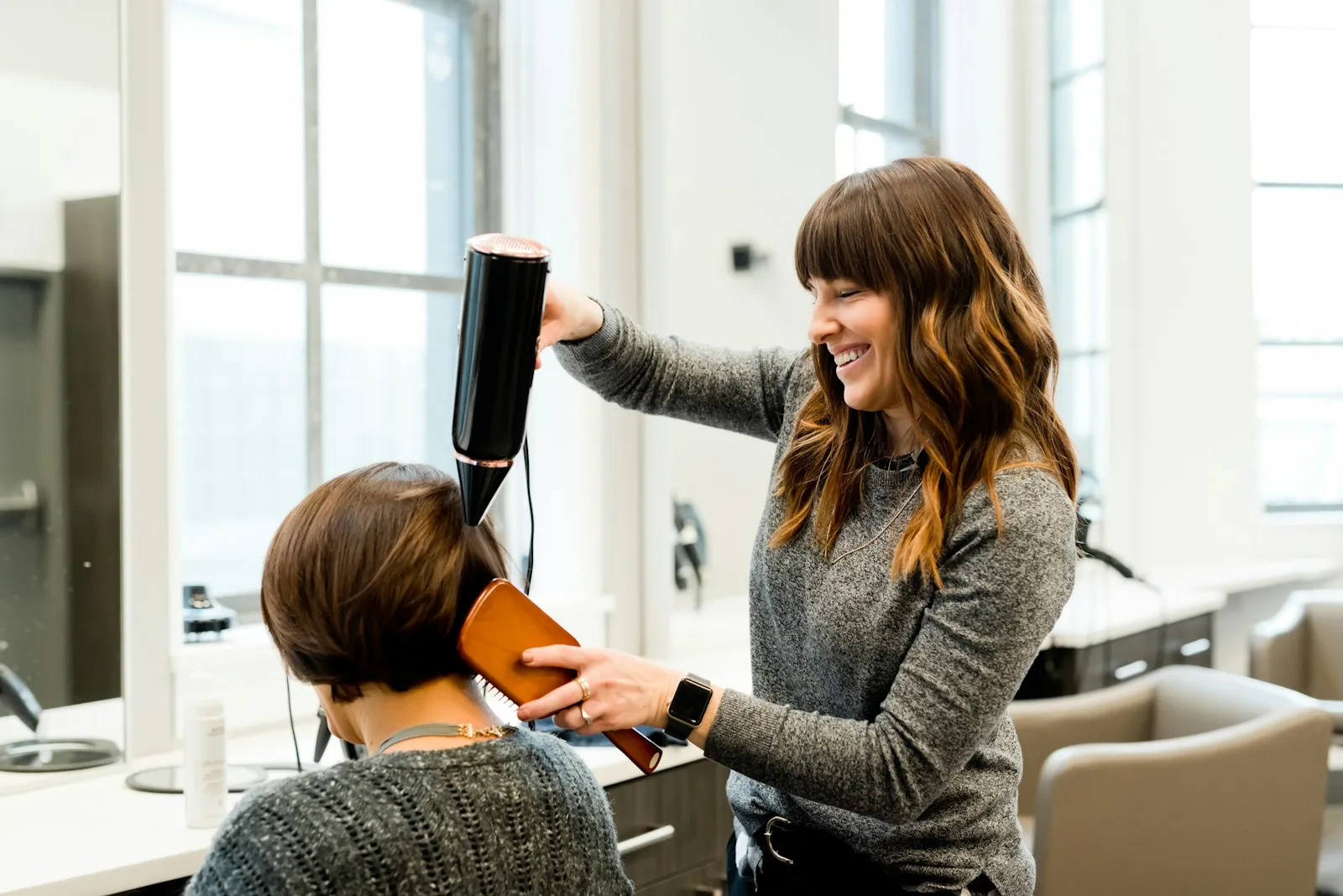 Friseurin föhnt einer Kundin die Haare im hellen Salon